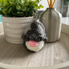 Crocheted gnome keychain on a wooden surface with plants in the background